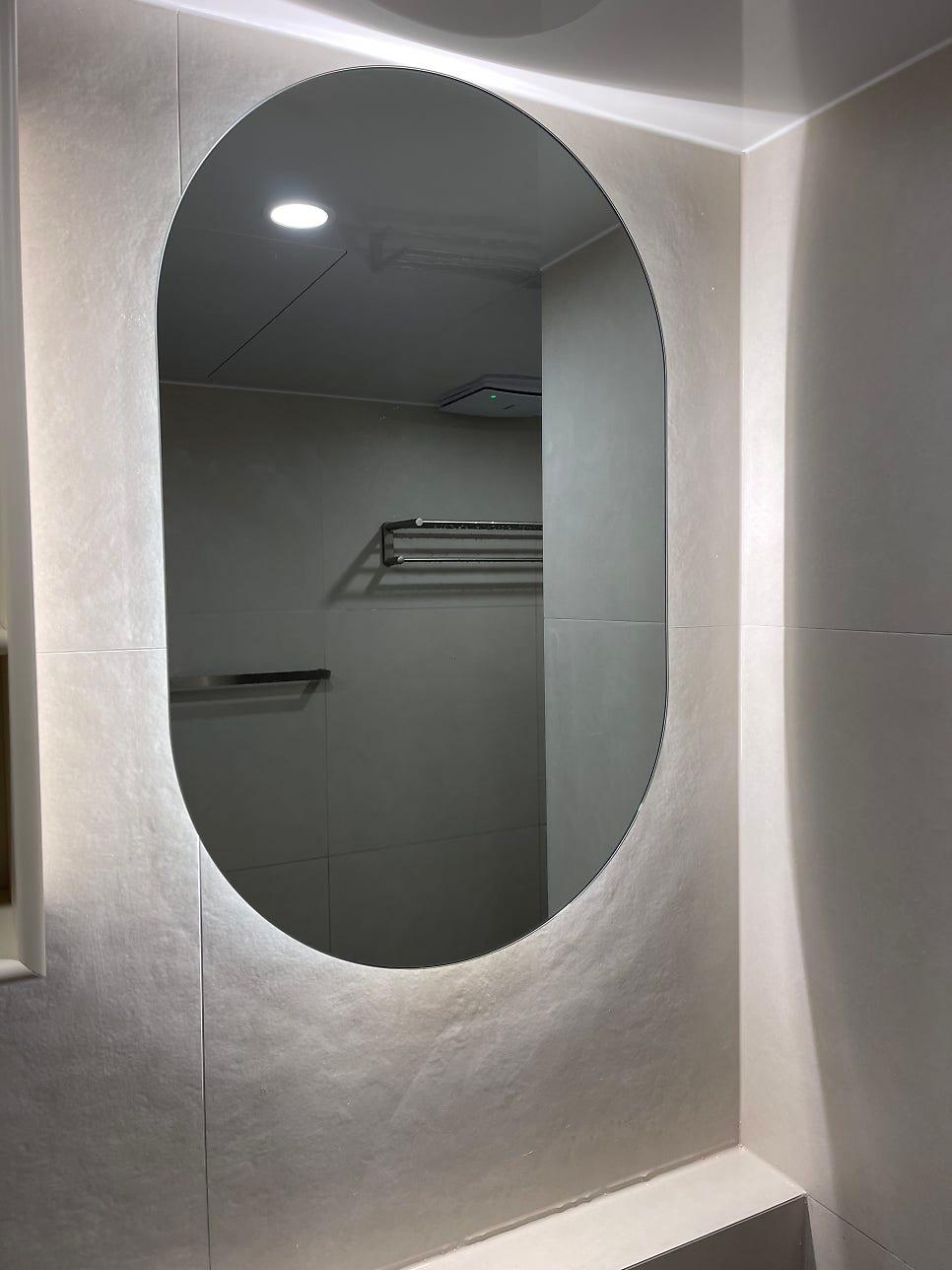 회색 타일 벽면과 타원형 조명 거울이 설치된 욕실