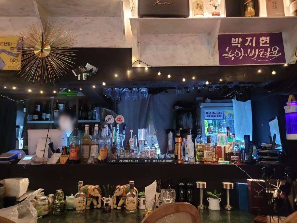 술병들이 진열된 바 카운터와 한글 배너가 있는 벽면