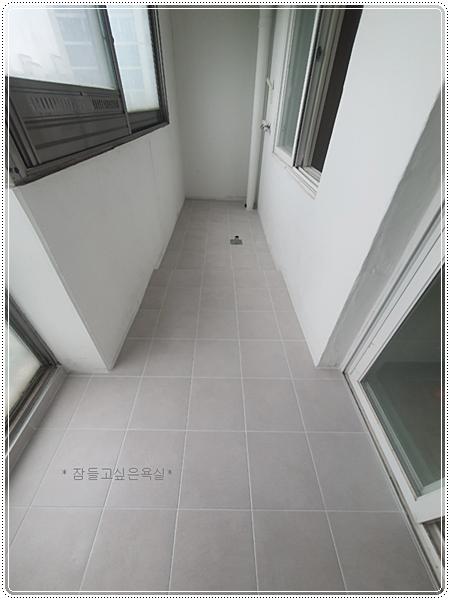 흰 벽면과 대비되는 회색 타일 바닥이 마감된 좁은 발코니 공간