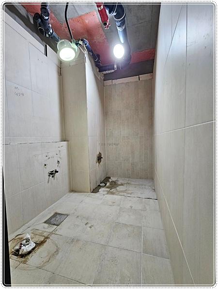 흰색 타일 벽면과 천장 배관이 보이는 시공 중인 공간