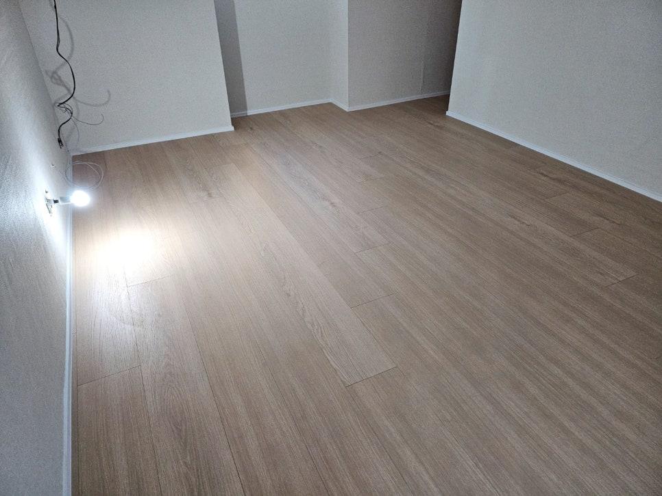 우드톤 마루와 흰색 벽지가 마감된 방