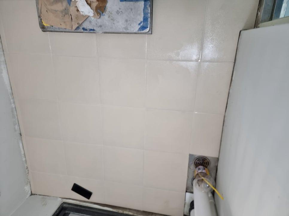 금속 프레임과 배수구가 보이는 흰색 타일 벽