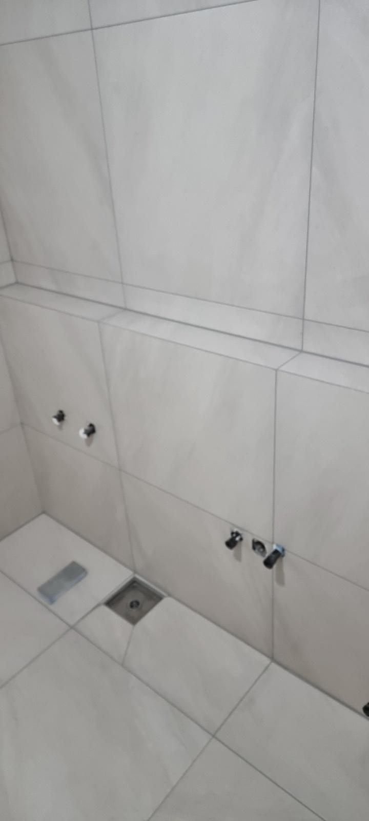 수전 및 배수구 부품이 설치된 흰색 타일 벽면