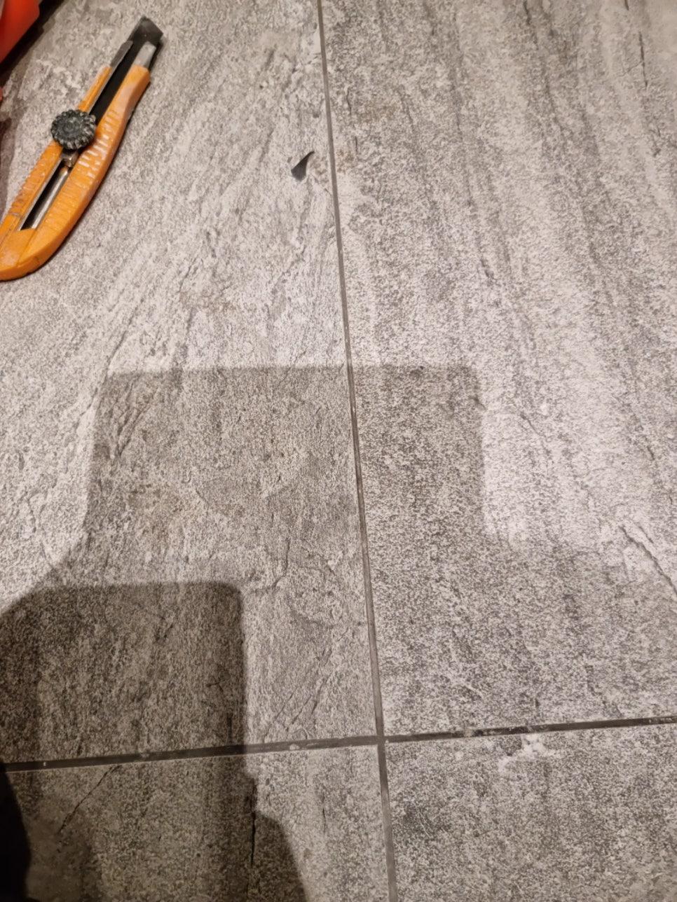회색 타일 바닥 위 오렌지색 테이프 커터가 놓인 모습