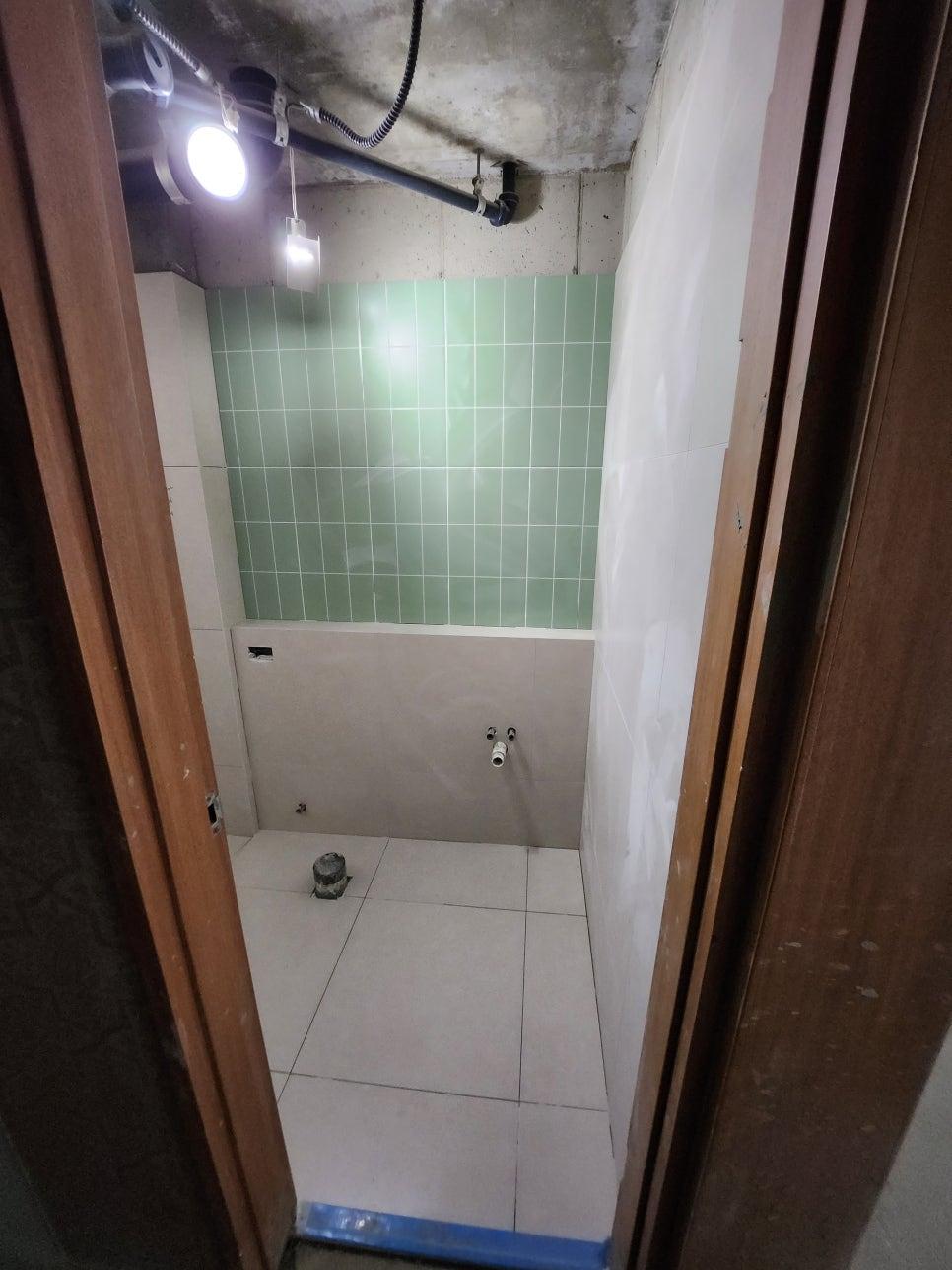천장 배관이 노출된 녹색 타일 벽면 공간