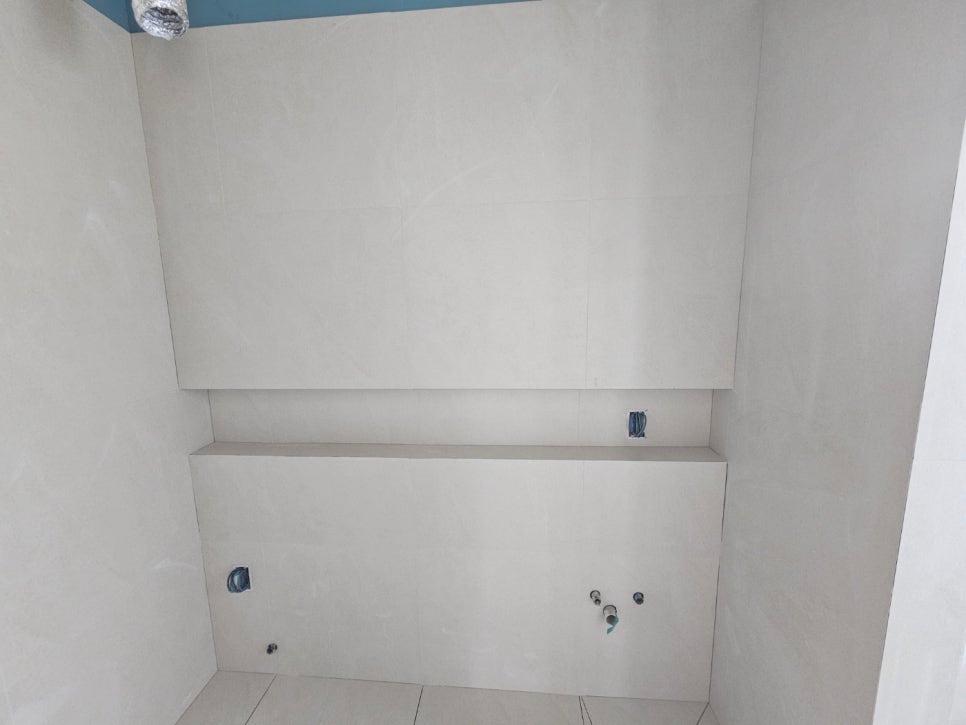 전기 및 배관 구멍이 보이는 흰색 타일 벽면