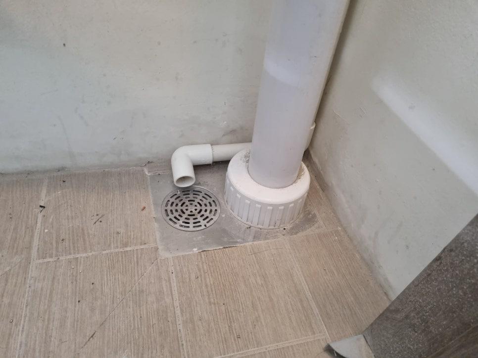 바닥 타일 위에 설치된 흰색 PVC 배관과 배수구