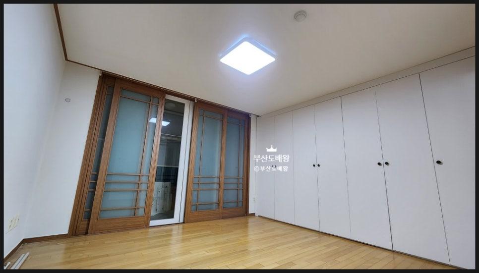 흰 벽, 목재 프레임의 유리문, 흰색 수납장, 목재 바닥재, 천장에 설치된 사각형 조명이 보이는 실내 공간