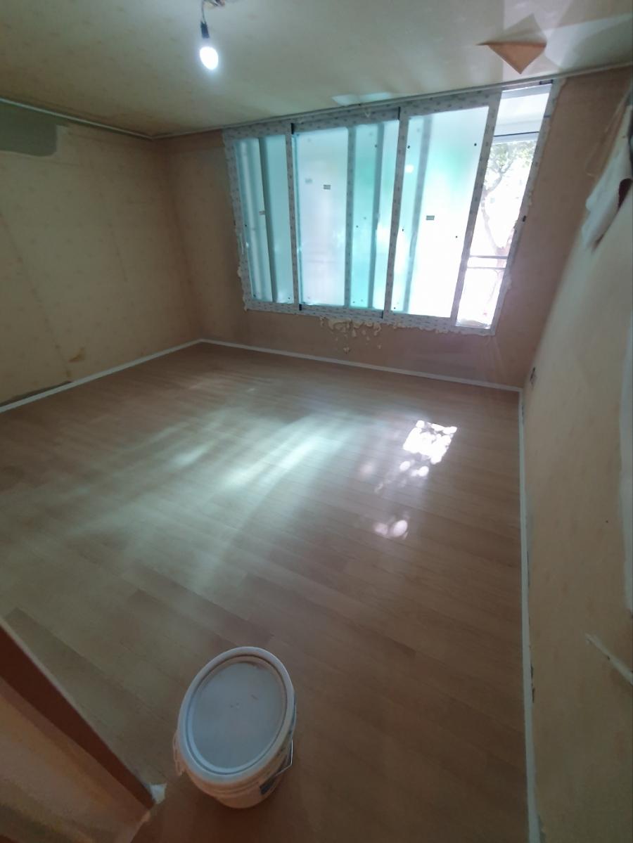 벽지가 벗겨진 벽면과 마감된 목재 마루가 보이는 모습