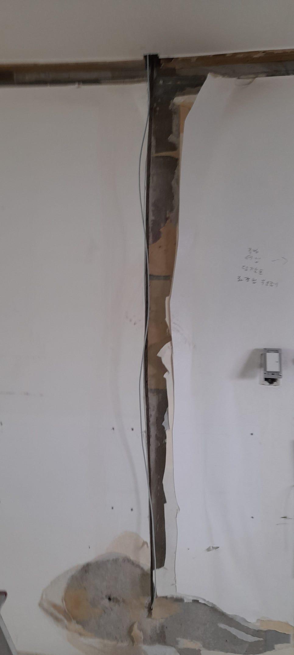 도배지가 벗겨지고 목재 구조물이 보이는 흰 벽