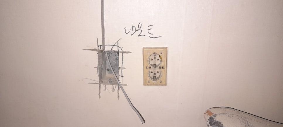 흰 벽면에 노출된 전선과 전기 박스 및 2구 소켓