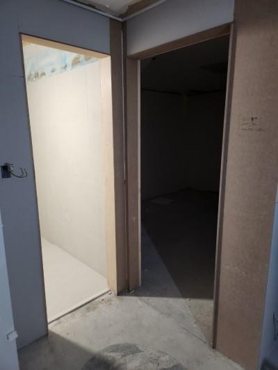 복도 공간, 벽면은 흰색과 회색 벽지로 마감, 바닥은 콘크리트, 문틀은 목재, 문이 열려 있는 상태