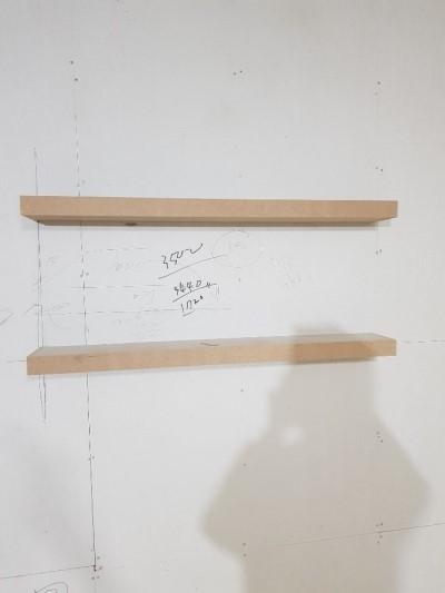 흰 벽면에 부착된 나무 선반과 시공 가이드 라인