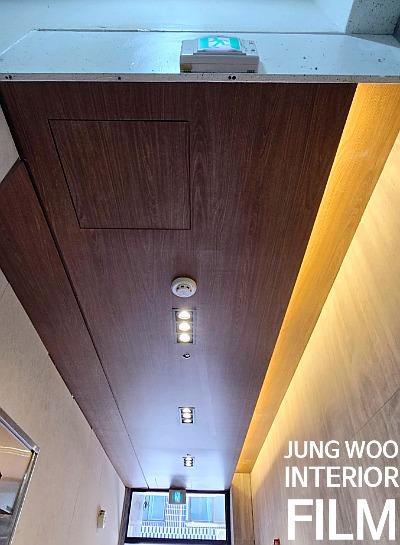 목재 패널 천장과 높은 벽면, 창문이 보이는 실내 공간