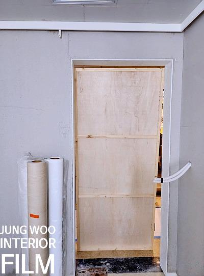 회색 벽돌 벽면에 설치 중인 흰색 프레임 문과 필름 롤