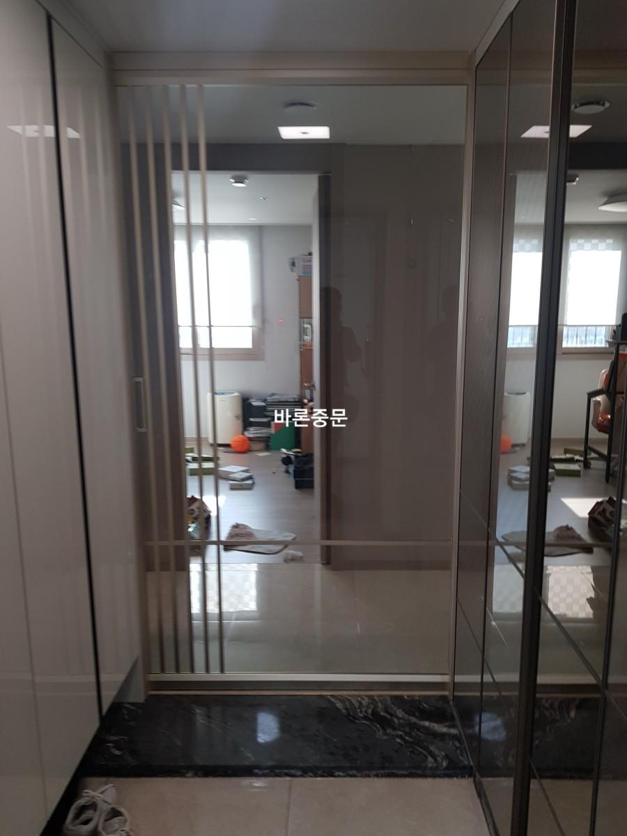 현관 타일 바닥 위에 설치 중인 유리 중문 프레임