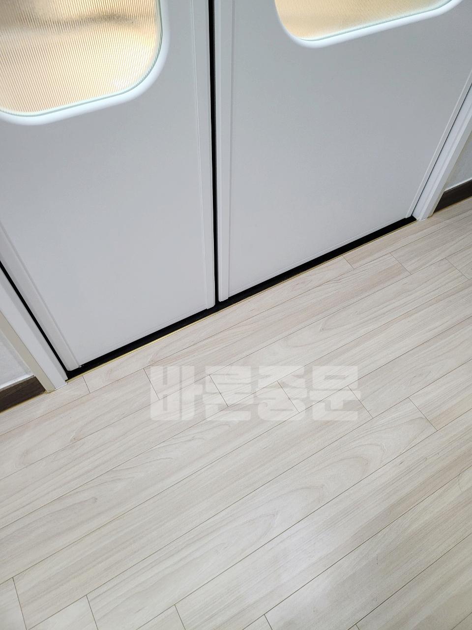 베이지 톤 목재 바닥과 조화를 이루는 화이트 도어