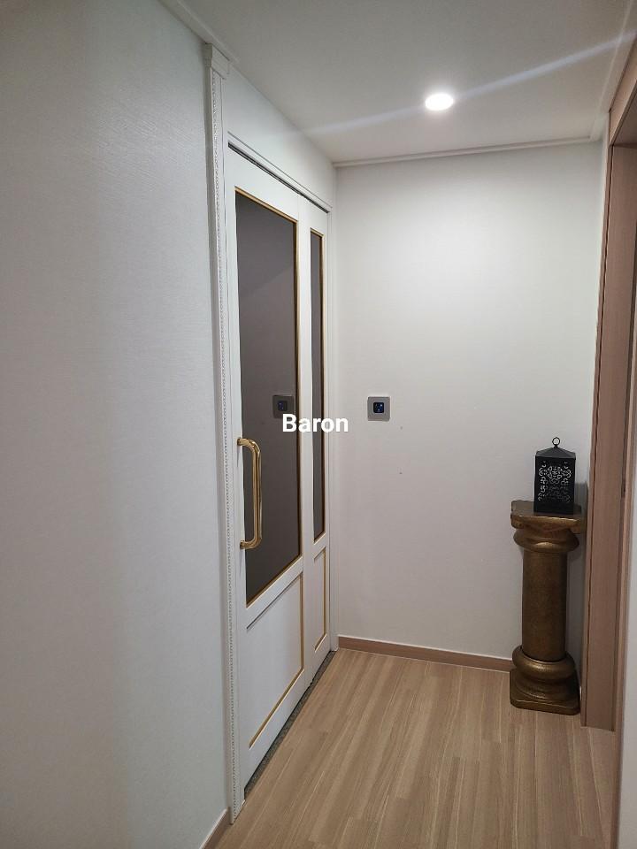 흰 벽, 흰색 도어(금색 장식), 금색 컬럼, 나무 바닥, 천장 조명, 벽에 설치된 스위치