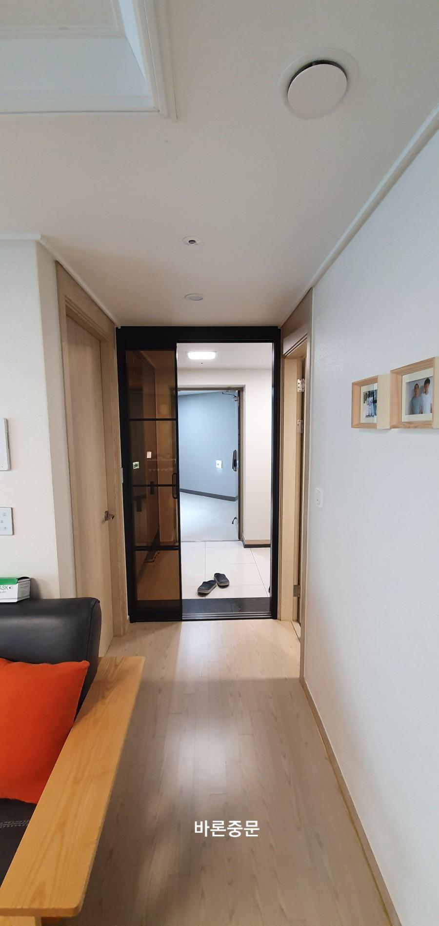 복도 쪽에서 바라본 블랙 프레임 유리문과 거실 풍경