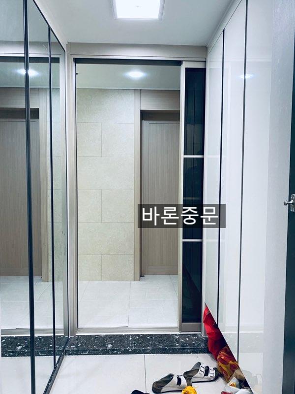 검은색 마감 벽 옆으로 설치된 유리문과 흰색 바닥 타일