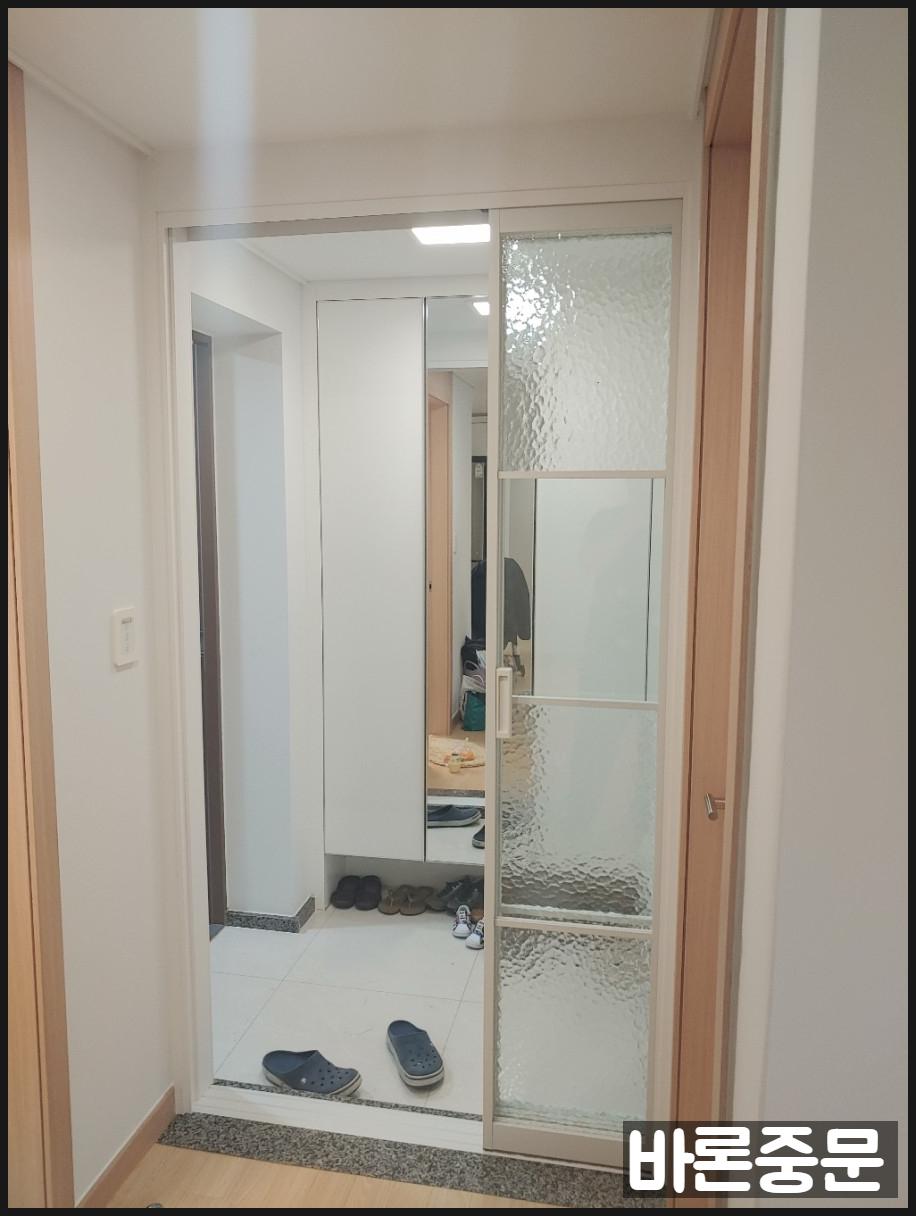 투명 유리 패널과 흰색 수납장이 보이는 현관
