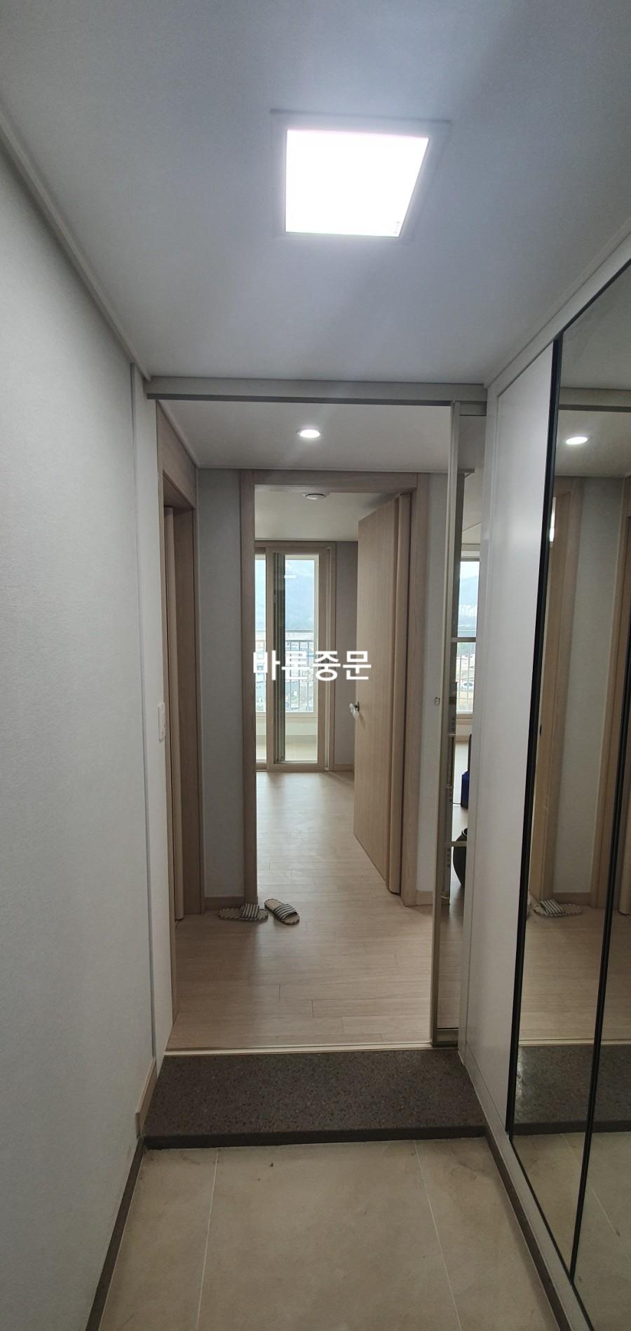 조명 아래 타일과 마루가 교차하는 복도 끝 중문