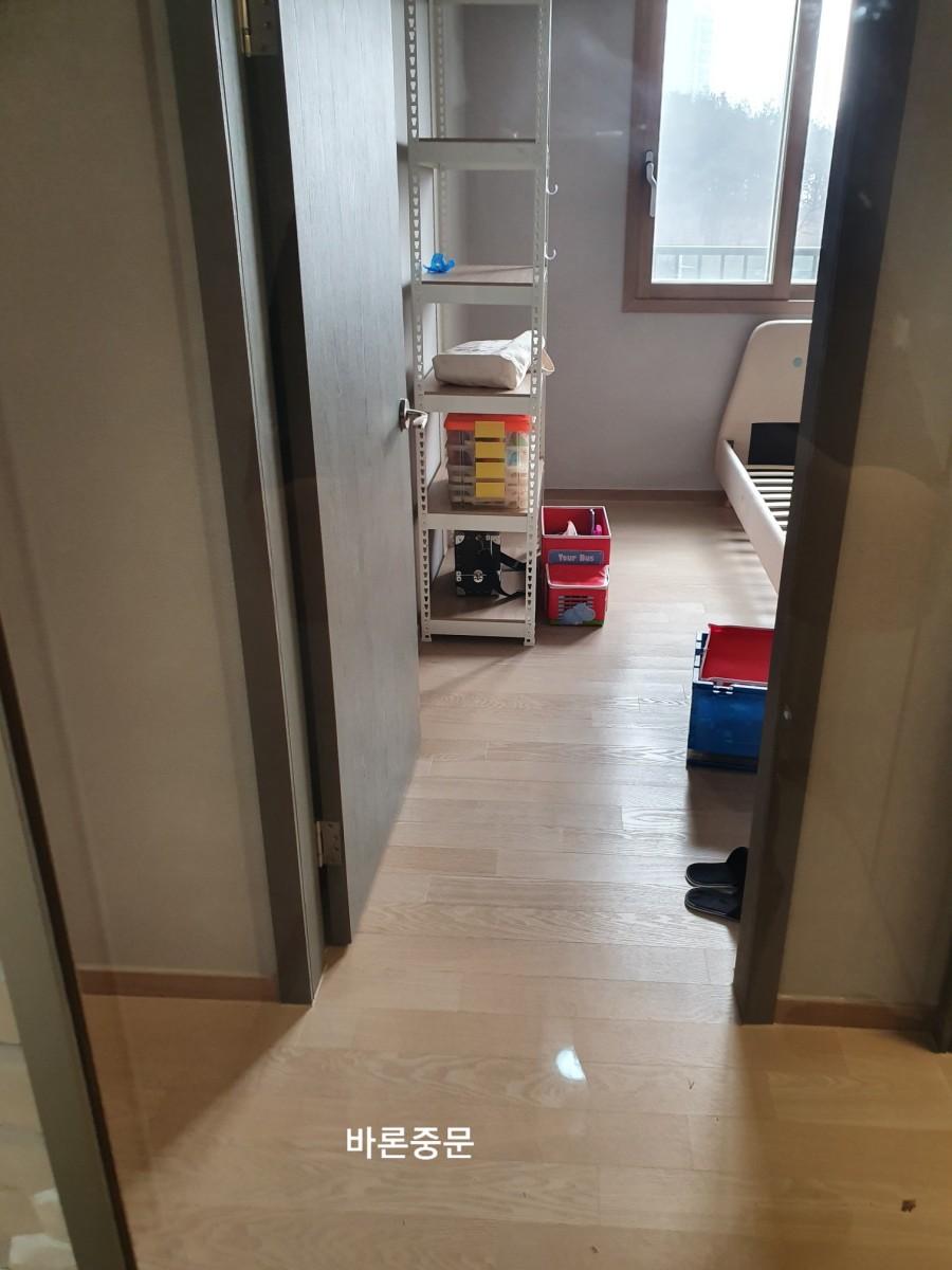 실내 공간에 흰색 금속 선반, 빨간색 및 파란색 상자, 베이비 침대, 창문, 목재 바닥이 보이는 아이방 내부