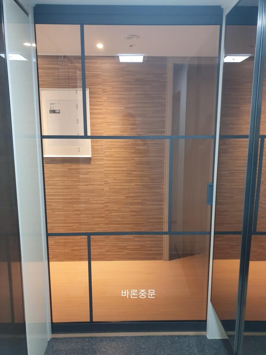 나무 패널 벽면과 천장 조명이 설치된 유리문 내부