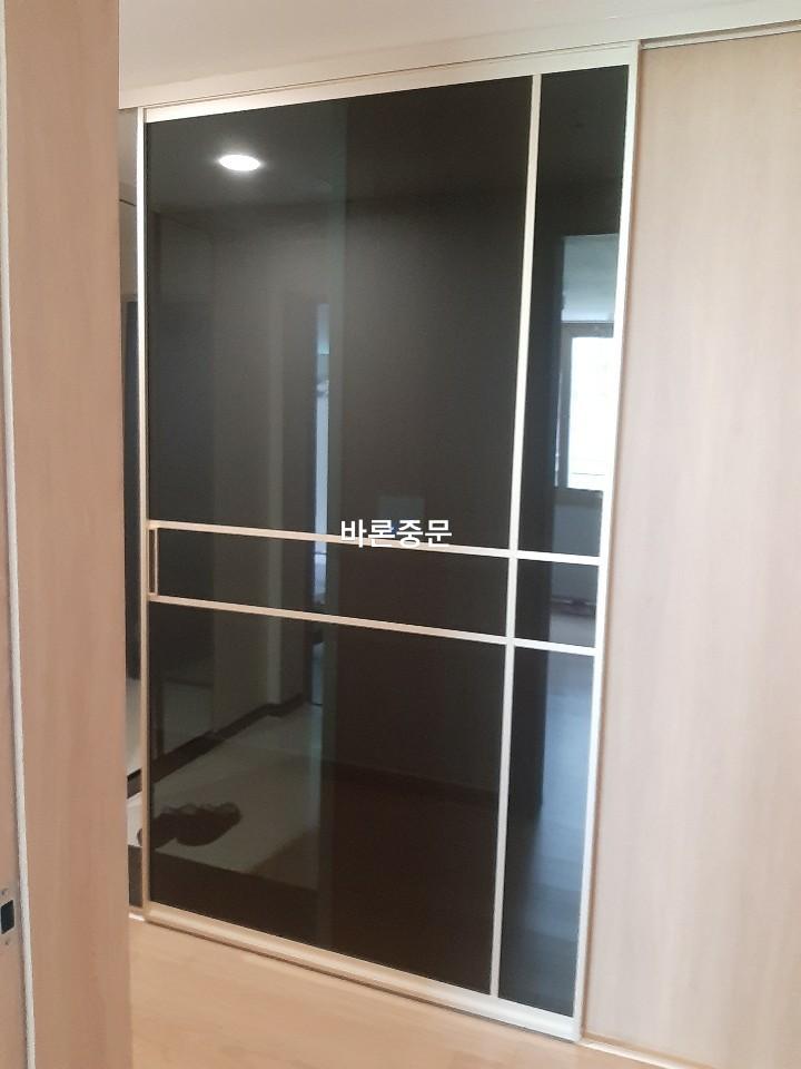조명 아래에서 광택이 드러나는 베이지색 패널과 검은 유리 도어