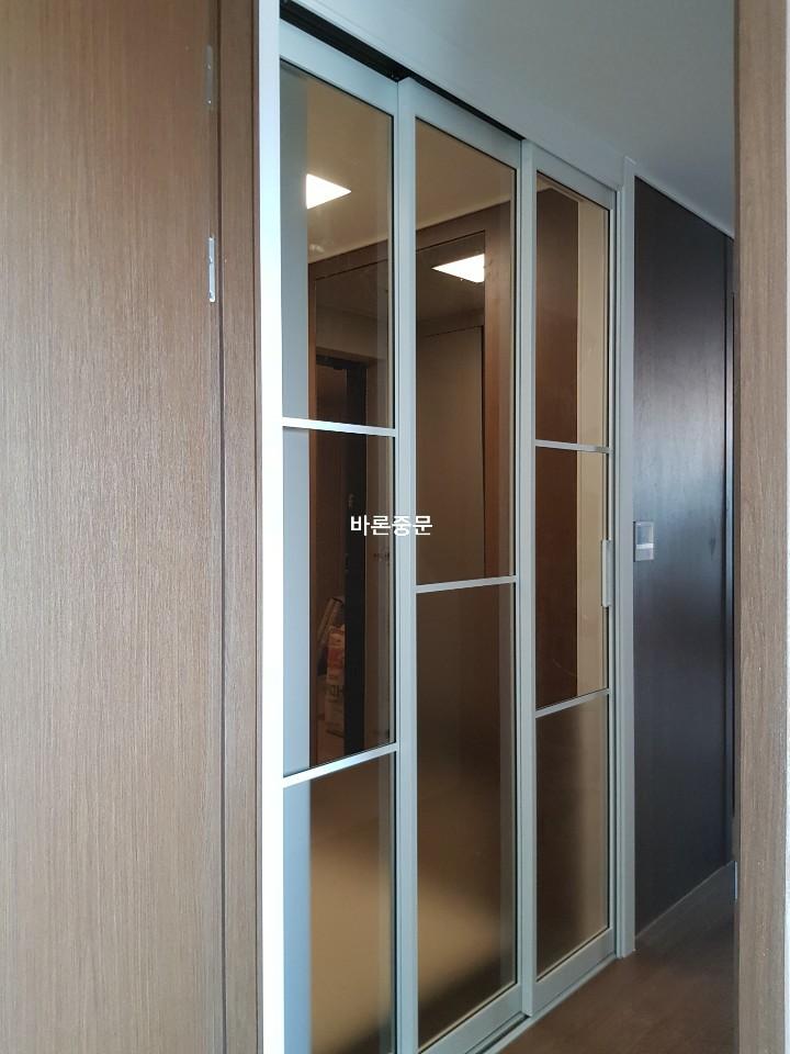빛이 투과되는 유리 패널 도어와 목재 및 검은색 패널 벽