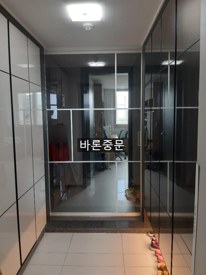 현관 복도 공간, 양쪽에 유리문으로 된 수납장, 바닥은 흰색 타일, 오른쪽 바닥에 신발이 놓여 있음