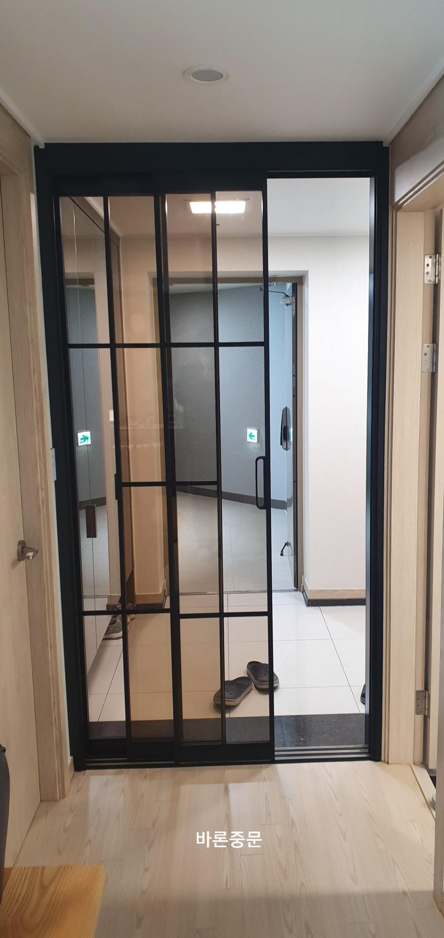 흰색 타일과 목재 바닥의 경계에 세워진 블랙 중문