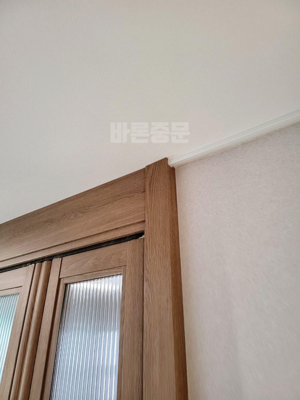 우드톤 도어 프레임과 실내 벽지의 상단 연결 부위