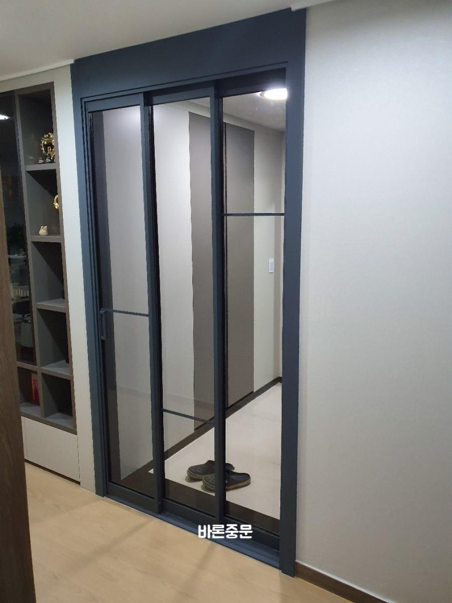 우드톤 벽면과 검은색 프레임 중문이 설치된 현관