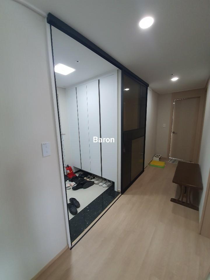 현관 내 화이트 수납장 옆에 배치된 블랙 유리문 시공 과정