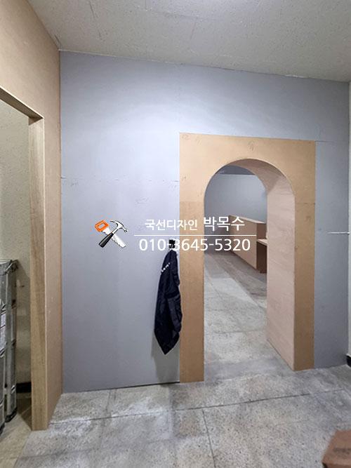 베이지색 아치형 문틀이 설치된 회색 벽면의 복도