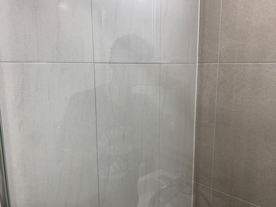 투명 유리 문 너머로 보이는 샤워부스 벽면