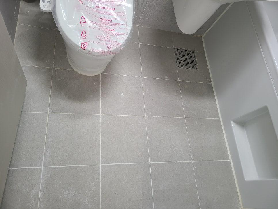 회색 타일 바닥과 흰색 세면대, 변기가 배치된 화장실