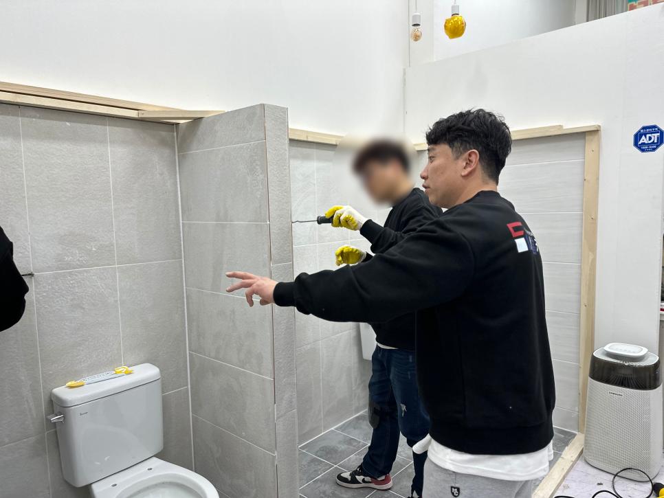 회색 타일 벽과 흰색 위생기구가 있는 욕실 공사 현장