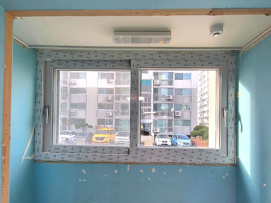 파란색 벽면에 흰색 프레임 창호가 설치 중인 모습