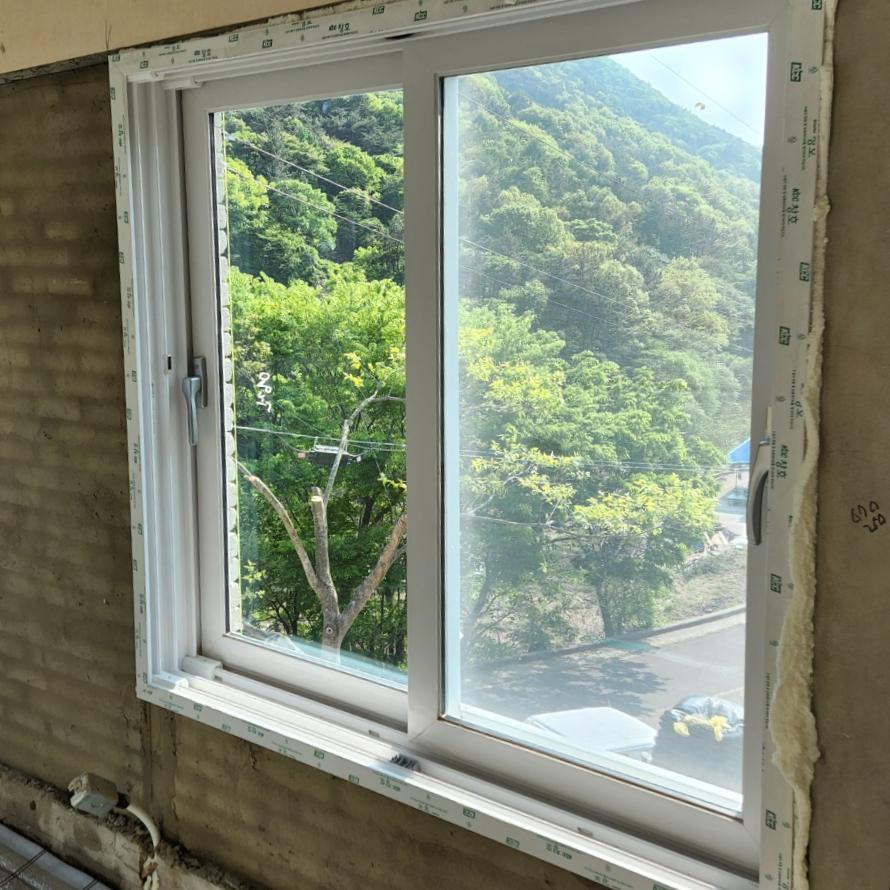 산과 나무가 보이는 창호 프레임 주변의 시공 흔적