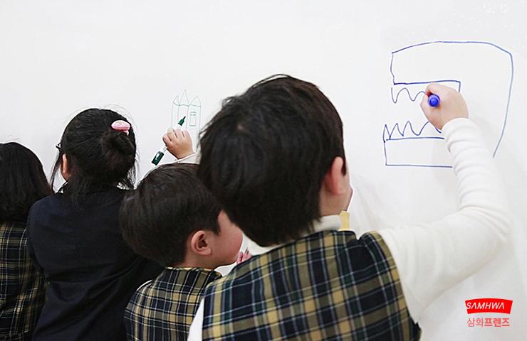 흰 벽면에 아이들이 펜으로 그림을 그리는 모습