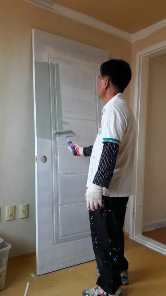 베이지색 벽면과 나무 마루가 있는 공간의 문 도색 작업