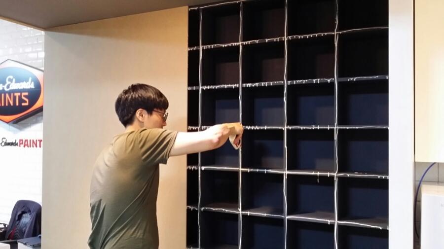 검은색 격자 수납장과 실내등이 설치 중인 벽면