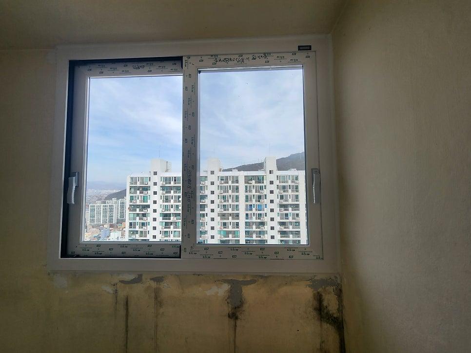 흰색 프레임 창호 너머로 보이는 아파트 단지와 산의 풍경