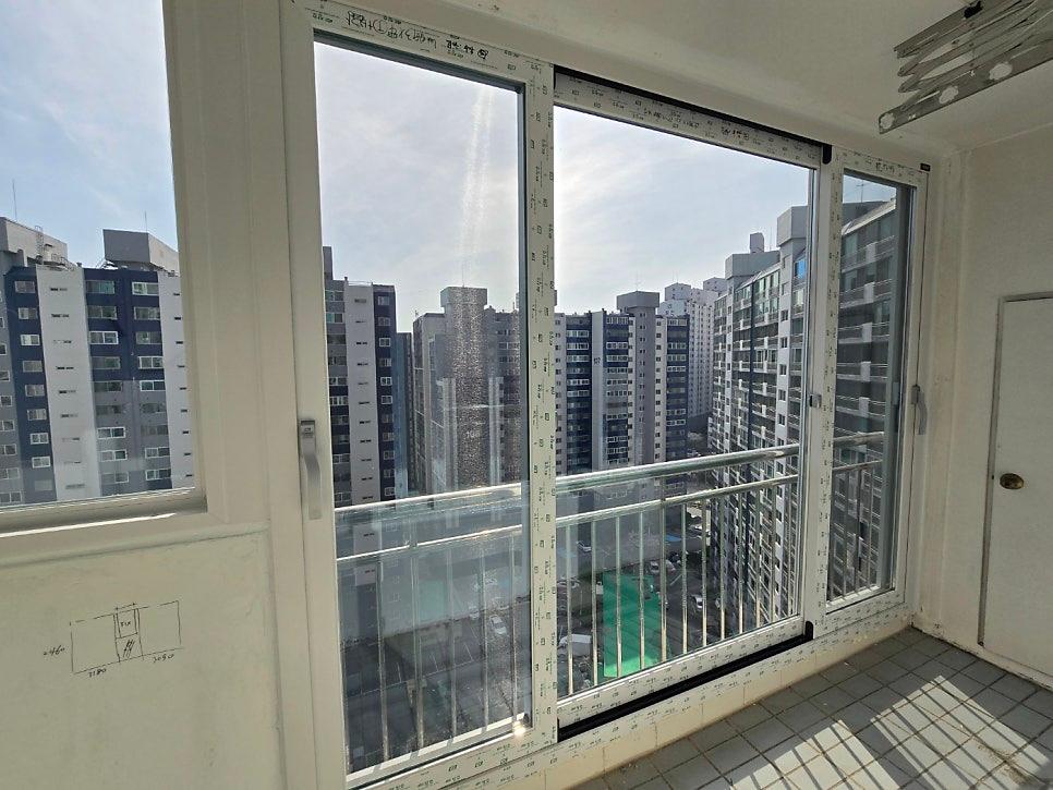 흰색 프레임 창호 너머로 고층 아파트가 보이는 발코니