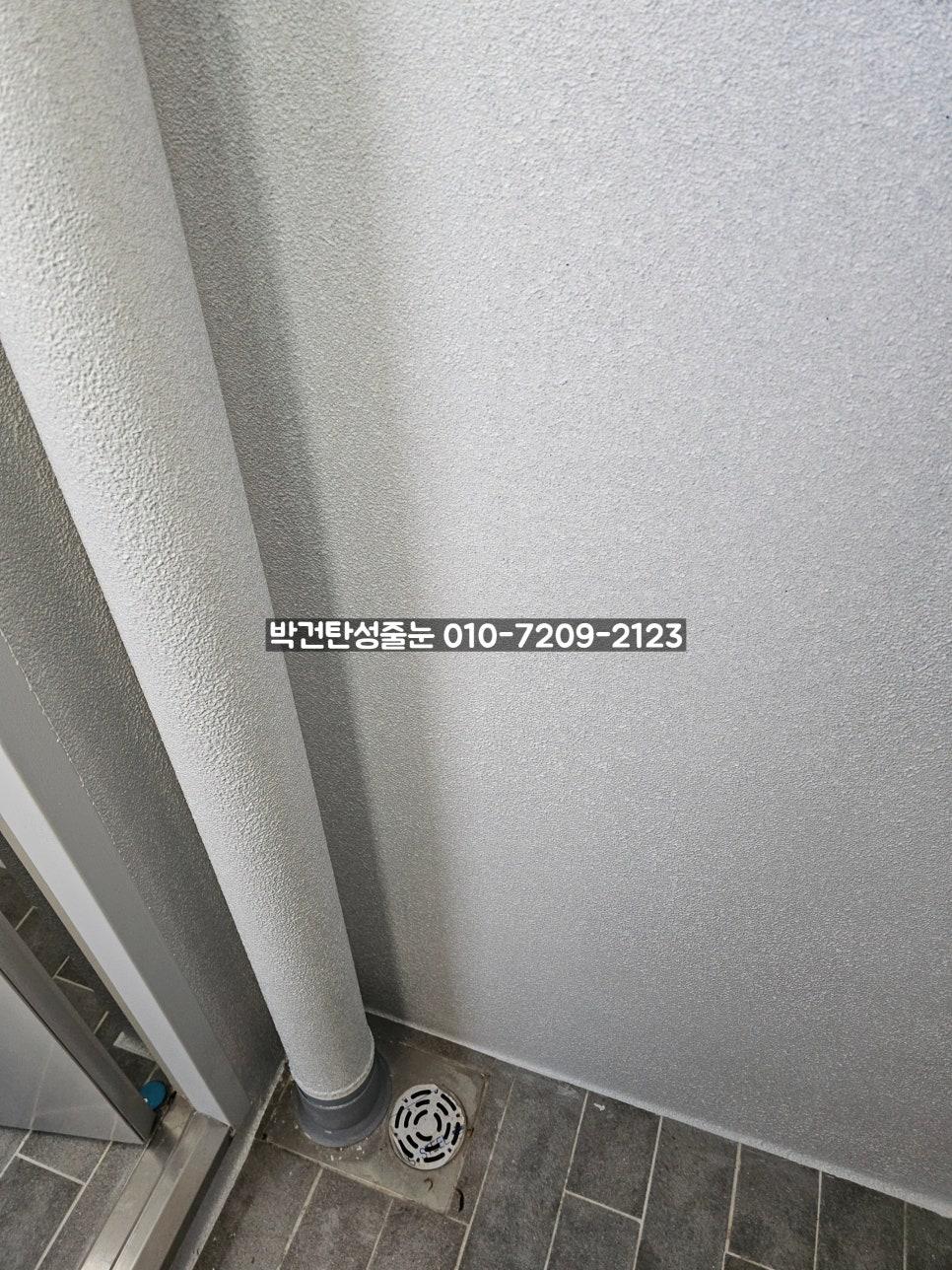 원형 배수구와 회색 파이프가 보이는 바닥과 벽 연결부