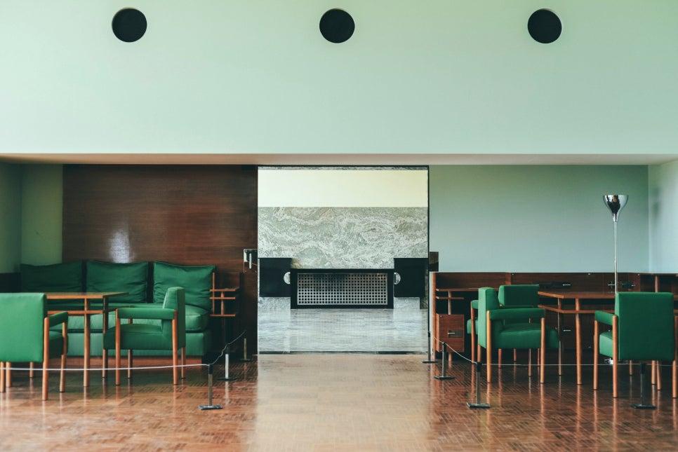 부드러운 조명 아래 그린 컬러 체어와 우드 테이블, 대리석 벽난로가 배치되어 미니멀한 무드를 더한 서재 공간이에요.