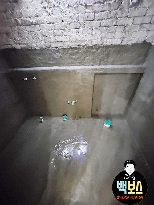 콘크리트 바닥에 물이 고여 있고 녹색 용기가 놓인 방