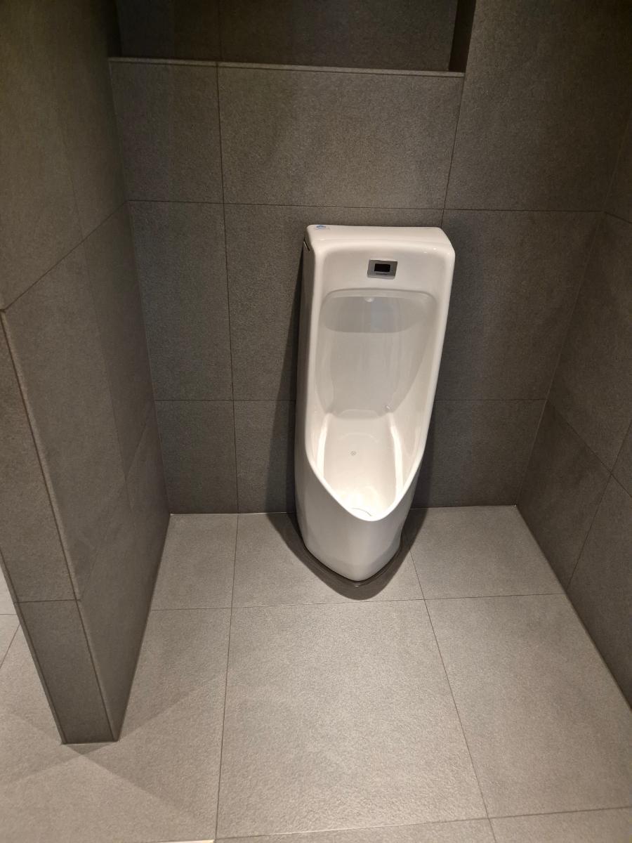 흰색 소변기가 설치된 회색 톤의 화장실